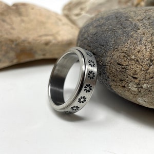 May include: A silver spinning ring with a pattern of black flowers around the band.
