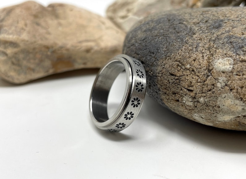 May include: A silver spinning ring with a pattern of black flowers around the band.