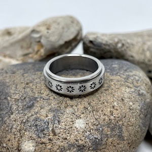 May include: A silver spinning ring with a band of small black flower designs.