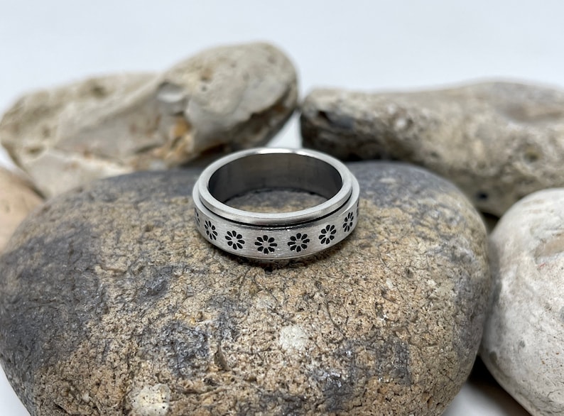 May include: A silver spinning ring with a band of small black flower designs.