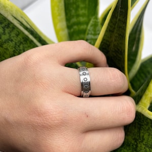 May include: A silver ring with a band of small, black flower designs.
