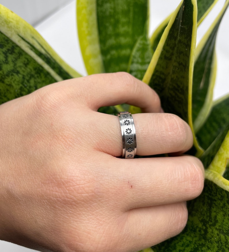 May include: A silver ring with a band of small, black flower designs.