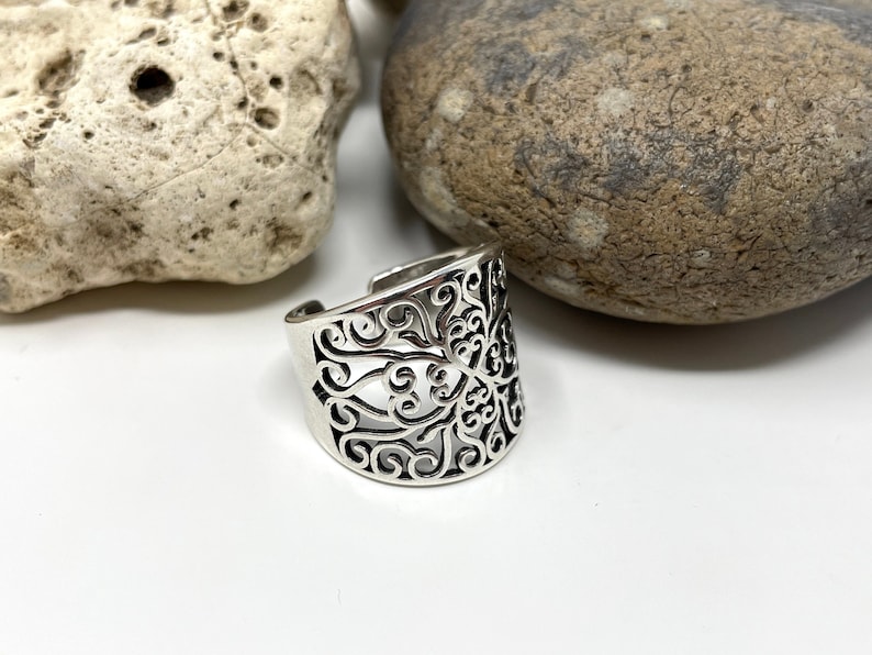 May include: A silver ring with a filigree design. The ring is wide and has a delicate, intricate pattern.