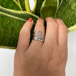 May include: A silver ring with a wavy, organic design. The ring is made of multiple bands that are stacked on top of each other.