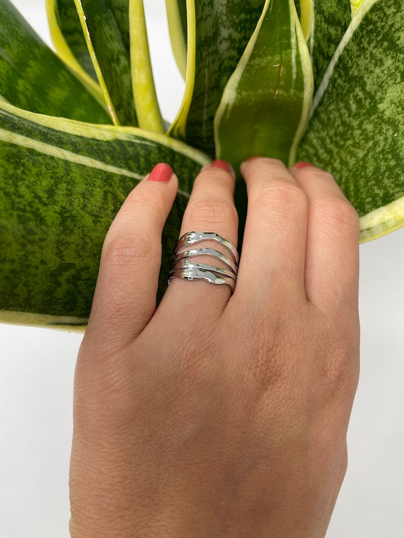 May include: A silver ring with a wavy, organic design. The ring is made of multiple bands that are stacked on top of each other.