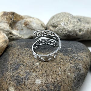 May include: A silver ring with a delicate, intricate design of overlapping floral patterns. The ring is open and adjustable, making it a versatile piece of jewelry.