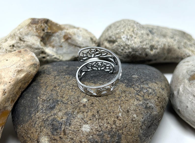 May include: A silver ring with a delicate, intricate design of overlapping floral patterns. The ring is open and adjustable, making it a versatile piece of jewelry.