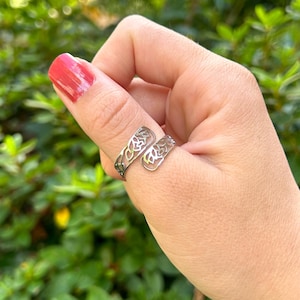 May include: A silver thumb ring with a delicate floral design. The ring is open and adjustable to fit most thumb sizes.