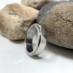 May include: A silver-colored ring with a grooved design. The ring is made of a shiny metal and has a smooth, polished surface. The ring is a simple, yet elegant piece of jewelry.