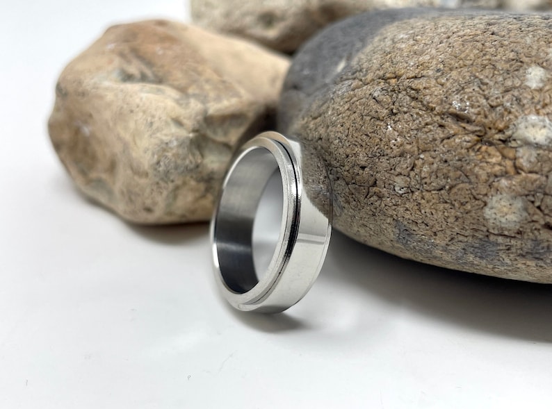 May include: A silver-colored ring with a grooved design. The ring is made of a shiny metal and has a smooth, polished surface. The ring is a simple, yet elegant piece of jewelry.