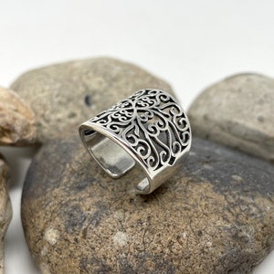 May include: A silver ring with a filigree design. The ring is open and adjustable.