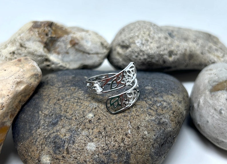 May include: A silver ring with a delicate, openwork design. The ring is twisted and features a floral pattern.