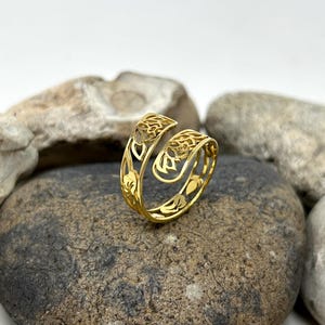 May include: A gold-colored ring with an intricate, openwork design featuring floral motifs. The ring is made of metal and has a delicate, feminine look.