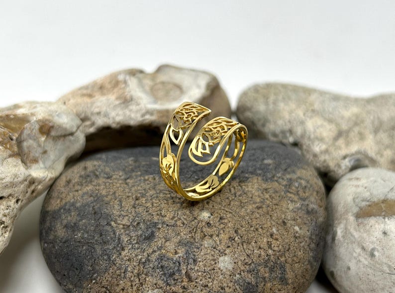 May include: A gold-colored ring with an intricate, openwork design featuring floral motifs. The ring is made of metal and has a delicate, feminine look.
