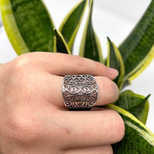 May include: A silver filigree ring with a wide band and intricate design.