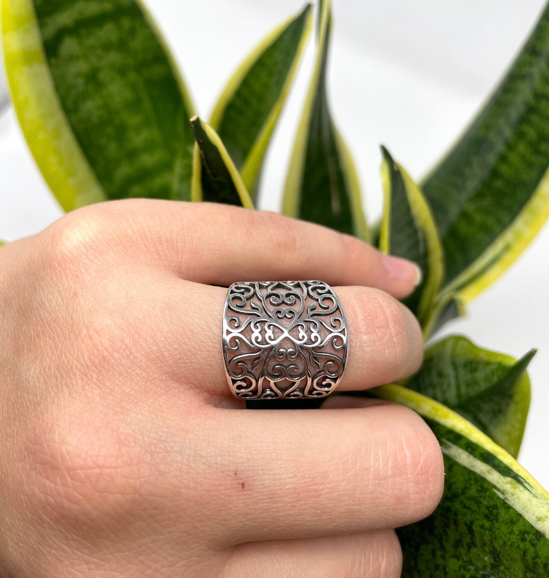 May include: A silver filigree ring with a wide band and intricate design.