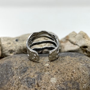May include: A silver ring with a textured, hammered finish. The ring has three bands that are stacked on top of each other.