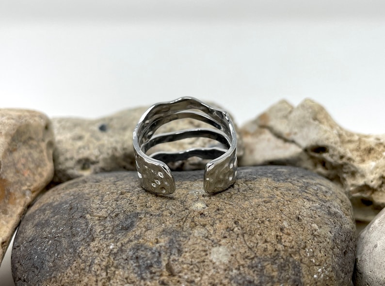 May include: A silver ring with a textured, hammered finish. The ring has three bands that are stacked on top of each other.