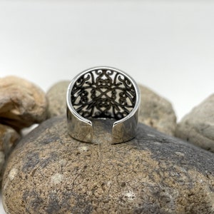 May include: Silver ring with an intricate openwork design. The ring is open in the back and has a smooth, polished finish.