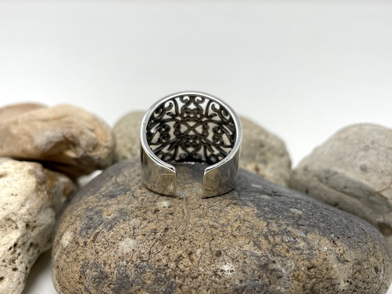 May include: Silver ring with an intricate openwork design. The ring is open in the back and has a smooth, polished finish.