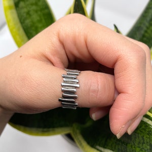 May include: A silver ring with a unique design featuring a series of vertical bars.