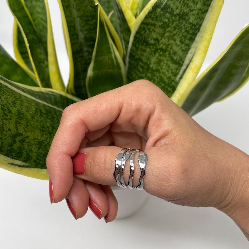 May include: A silver ring with a hammered texture. The ring is made of multiple bands that are stacked on top of each other. The ring is worn on a finger.