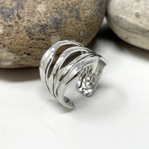May include: A silver ring with a wavy, textured design. The ring is open and adjustable.