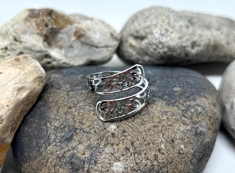 May include: A silver ring with a delicate, intricate design of swirling leaves. The ring is open and adjustable to fit different finger sizes.
