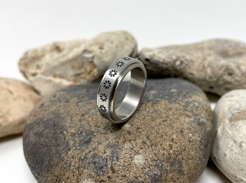 May include: A silver spinning ring with a pattern of small black flowers around the band.