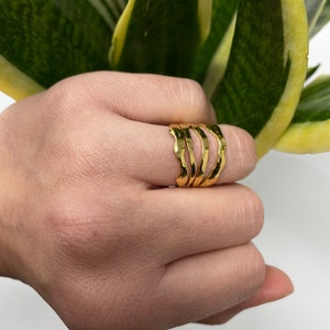 May include: Gold ring set with a wavy, textured design. The ring is worn on a finger.