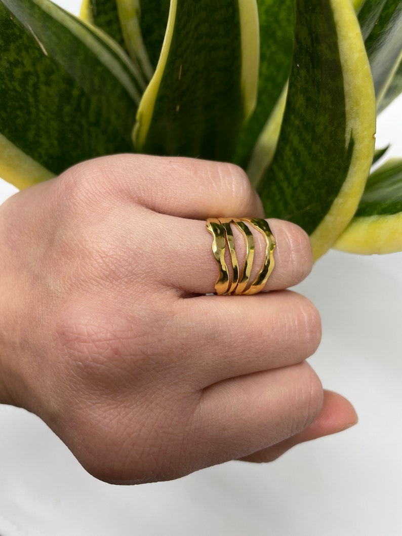 May include: Gold ring set with a wavy, textured design. The ring is worn on a finger.