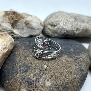 May include: A silver toe ring with a Celtic knot design. The ring is on a gray rock.