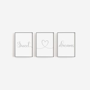 May include: Three black framed prints with white backgrounds. The left print has the word "sweet" in gray cursive script. The middle print has a gray heart drawn with a continuous line. The right print has the word "dreams" in gray cursive script.