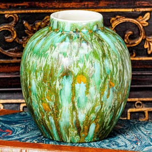 May include: A round ceramic vase featuring a glossy glaze with vertical streaks of emerald green, light turquoise, and earthy brown tones. The vase has a short, narrow neck with a smooth white interior rim and a bulbous, ribbed body shape.
