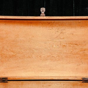 Puede incluir: Cofre de madera abierto con acabado marr&oacute;n claro. El cofre tiene forma rectangular con tapa con bisagras y cierre met&aacute;lico. La veta de la madera es visible y el cofre parece estar vac&iacute;o.