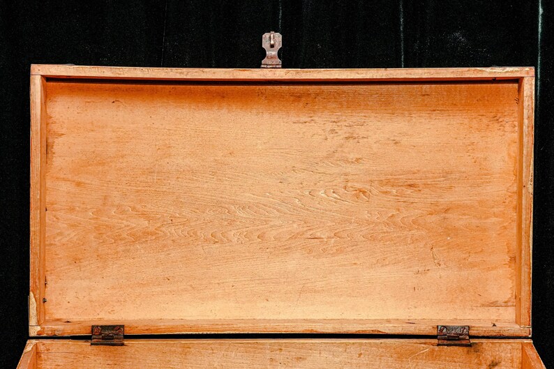 Puede incluir: Cofre de madera abierto con acabado marr&oacute;n claro. El cofre tiene forma rectangular con tapa con bisagras y cierre met&aacute;lico. La veta de la madera es visible y el cofre parece estar vac&iacute;o.