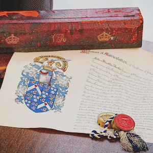 May include: A weathered red wooden box with gold crown emblems and the letters VR, placed behind a document titled Extract of Matriculation. The document features a blue and white coat of arms, black cursive text, and a red wax seal with a blue and white cord.