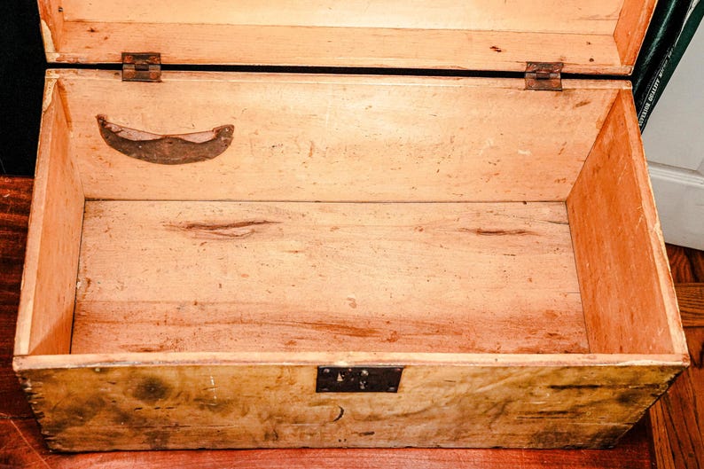 Puede incluir: Cofre de madera abierto de forma rectangular, con tapa con bisagras y herrajes met&aacute;licos. El interior est&aacute; vac&iacute;o, revelando la veta y el color natural de la madera. Una manija de metal est&aacute; fijada a la tapa.