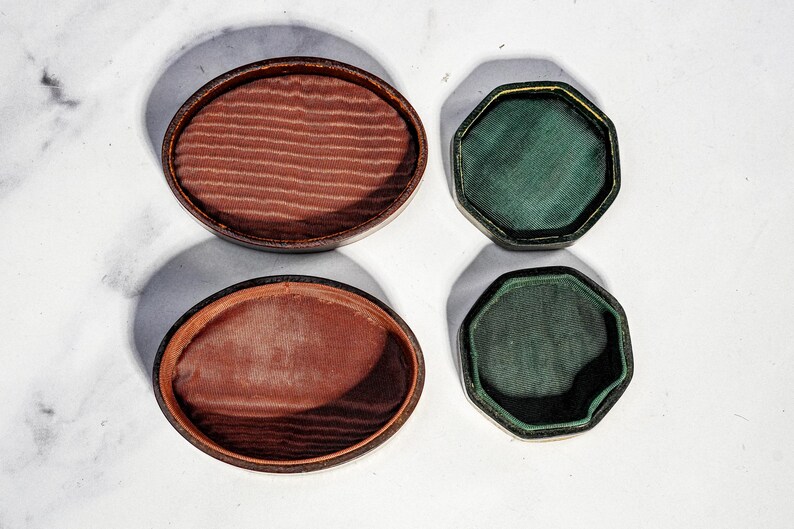 May include: Two oval-shaped containers with dark brown exteriors and textured reddish-brown fabric linings, alongside two octagonal-shaped containers with dark green exteriors and smooth dark green fabric linings, all viewed from directly above.