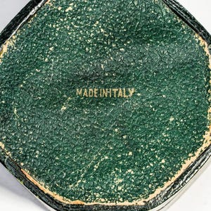 May include: A hexagonal object with a textured dark green surface featuring a gold-coloured border and the text MADE IN ITALY printed in the centre. The object has a worn appearance with visible signs of age along the edges and the green surface.