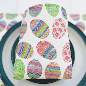 May include: White linen napkin featuring a colourful Easter egg design. The eggs are decorated with a variety of colours, including red, blue, green, yellow, and pink.
