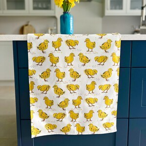 May include: A white kitchen towel with a yellow chick pattern. The towel is hanging on a blue cabinet door.