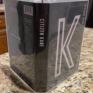 May include: A Criterion Collection edition of the film "Citizen Kane" in a clear plastic case. The cover is black with the title in white and a large white "K". The spine also displays the title. The back of the case lists details about the film.