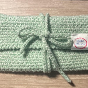 Peut inclure: Pochette crochetée vert menthe avec fermeture à nouer assortie. Le sac fait main présente un motif de point texturé et une petite étiquette avec le texte "Chloe Maestria". La pochette est pliée et nouée avec un cordon assorti.