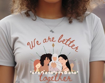 May include: A light gray t-shirt with the text "We are better together" in a warm brown script. The graphic features diverse women figures. The shirt is a crew neck style.