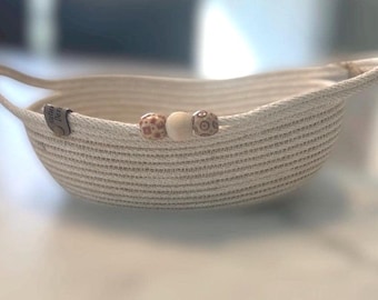 May include: A white rope bowl with three decorative beads. The beads are brown, white, and brown with white circles. The bowl has two handles and a small tag that says "Hello Dear".