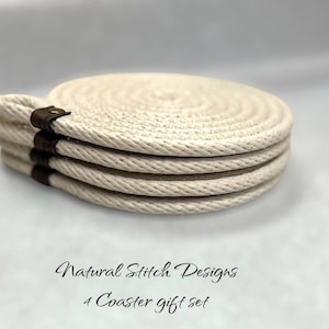 May include: Set of four round natural woven coasters with brown leather trim. The coasters are stacked on top of each other. The text "Natural Stitch Designs 4 Coaster gift set" is printed below the coasters.
