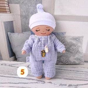 5. May include: Handmade doll wearing lavender jumpsuit with owl sticker and white hat. Doll has closed eyes and smiling face. Doll wears silver necklace with white pendant. Doll measures approximately 20 cm tall.