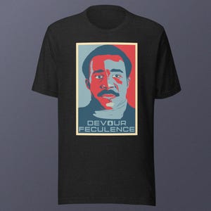 Puede incluir: Una camiseta negra con un gráfico rojo, blanco y azul de un hombre con bigote y el texto "DEVOUR FECULENCE".