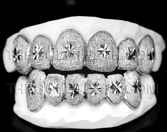 May include: Silver grill with diamond-shaped stones and a star design. The grill is displayed on a white mold.